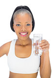 Fit woman holding glass of water while looking at camera