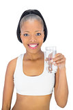 Smiling woman in sportswear holding glass of water while looking at camera