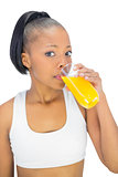Fit woman drinking glass of orange juice while looking at camera