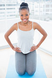 Smiling woman sitting on exercise mat with hands on hip