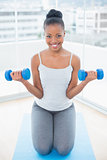 Fit woman sitting on exercise mat and working out with dumbbells