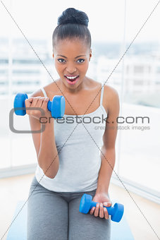 Woman sitting on exercise mat working out with dumbbell