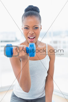 Fit woman working out wit h dumbbell while looking at camera