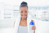 Fit smiling woman with towel around her neck holding sports bottle