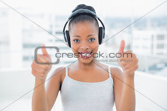 Smiling woman listening to music with headphones and giving thumbs up