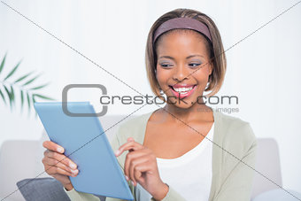 Happy woman sitting on sofa using her tablet