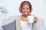 Smiling woman sitting on sofa holding mug of coffee