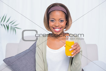 Smiling woman sitting on sofa holding glass of orange juice