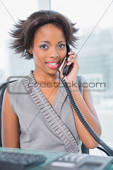Smiling businesswoman sitting on her desk calling on phone