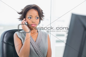 Serious woman talking on phone while looking at computer screen