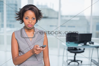 Unsmiling businesswoman standing in her office and texting