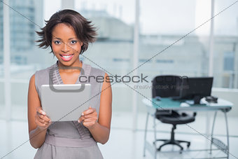Smiling businesswoman standing in her office and holding tablet