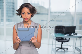 Serious businesswoman standing in her office holding tablet