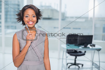 Smiling businesswoman standing in her office holding pen