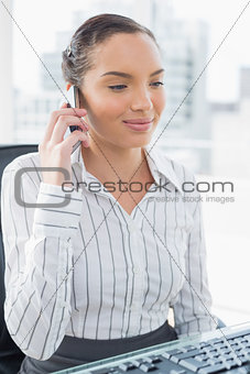 Happy businesswoman calling on phone while looking at computer screnn