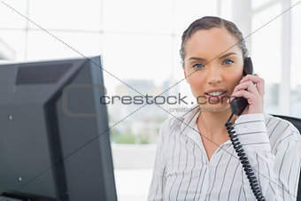 Pretty businesswoman talking on telephone while looking at camera