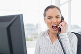 Angry businesswoman screaming on telephone while looking at camera