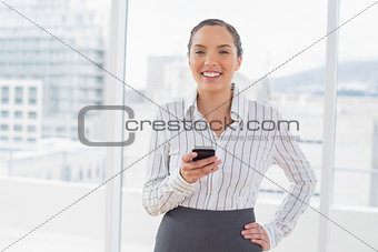 Happy businesswoman standing in her office and texting