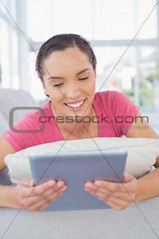 Happy woman lying on sofa and using tablet