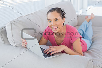 Smiling brunette using her laptop on the couch