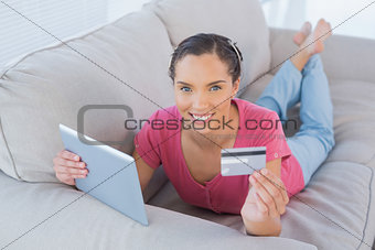 Casual woman lying with a credit card and a tablet