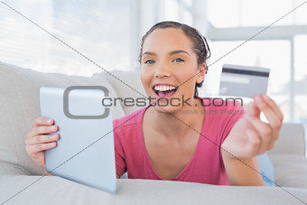 Attractive woman lying on a sofa holding a card and tablet