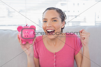 Smiling woman sitting on sofa and holding piggy bank