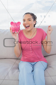 Happy woman sitting on sofa showing piggy bank