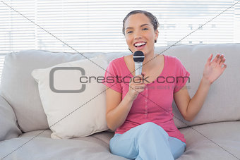 Brunette sitting on her sofa singing into microphone looking at camera
