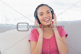 Happy woman sitting on sofa with headphones on and listening to music