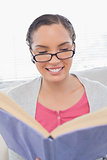 Happy woman with reading glasses sitting on sofa and reading a book