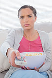 Serious woman eating popcorn while watching tv
