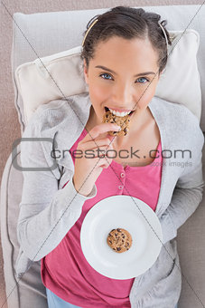 Smiling woman lying on sofa eating cookie