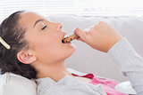 Side view of peaceful woman lying on sofa and eating a cookie