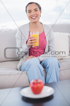 Cheerful woman sitting on sofa holding orange juice