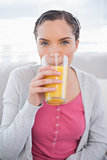 Attractive woman sitting on sofa drinking orange juice