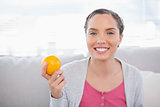 Cheerful woman sitting on sofa and holding orange