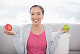 Smiling woman sitting on sofa holding green and red apple