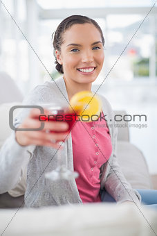 Smiling woman sitting on sofa and showing cocktail