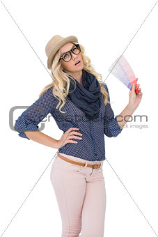 Thinking trendy blonde with classy glasses holding color chart