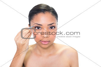 Concentrated young dark haired model plucking her eyebrows