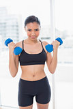 Dynamic dark haired model in sportswear exercising with dumbbells