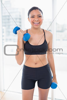 Laughing dark haired model in sportswear exercising with dumbbells