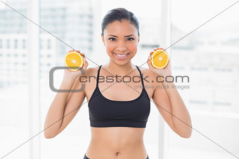 Beautiful dark haired model in sportswear holding orange halves