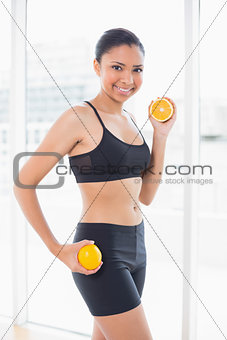 Dynamic dark haired model in sportswear holding orange halves