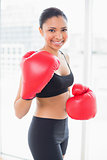 Amused dark haired model in sportswear wearing red boxing gloves