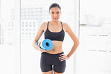 Serious dark haired model in sportswear carrying a blue exercise mat