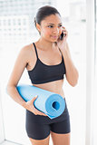 Healthy dark haired model in sportswear carrying an exercise mat and making a phone call
