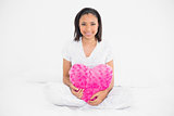Pleased young dark haired model holding a heart-shaped pillow