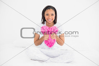 Content young dark haired model cuddling a heart-shaped pillow
